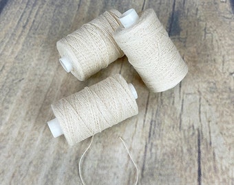 Puede incluir: Tres carretes de hilo de algodón blanco natural sobre una superficie de madera.