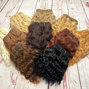 May include: A variety of human hair wefts in different colors and textures, including blonde, brown, red, and black. The wefts are arranged in a circle on a wooden surface.