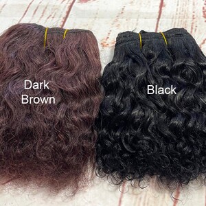 May include: Two bundles of curly human hair extensions, one dark brown and one black. The bundles are tied together with rubber bands.