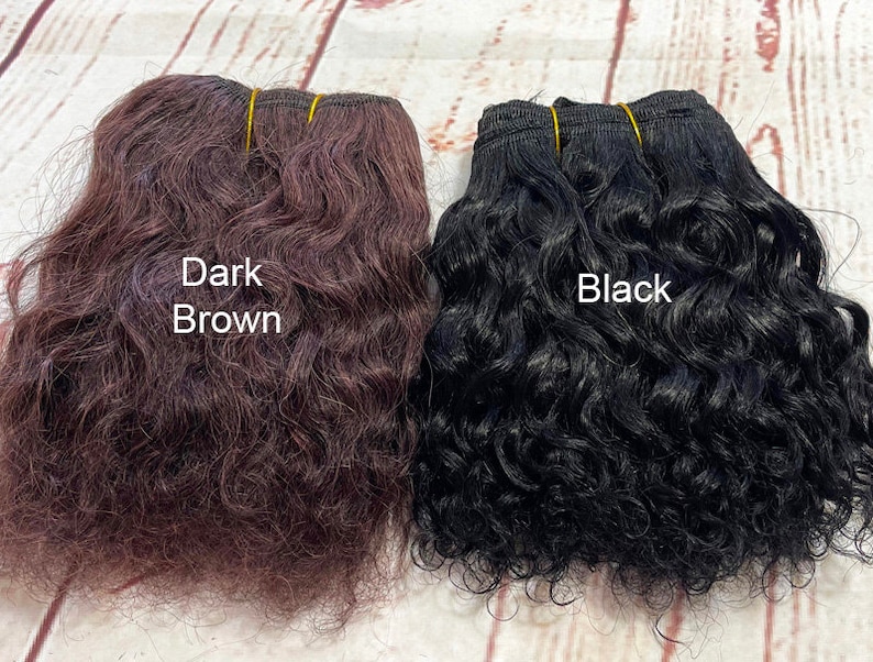 May include: Two bundles of curly human hair extensions, one dark brown and one black. The bundles are tied together with rubber bands.