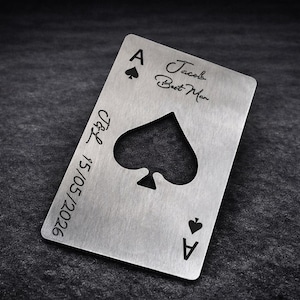 May include: A silver-coloured metal bottle opener shaped like a playing card, specifically the Ace of Spades. The card features a cutout spade symbol in the centre, the text Jacob Best Man, and the engraved date 15/05/2026 with the initials J&L.