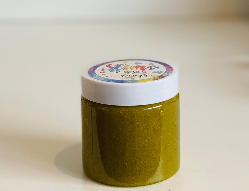 Pode incluir: Um pequeno frasco de slime verde com um r&oacute;tulo colorido que diz "Slime" e "Eggos May" em uma fonte caprichosa.