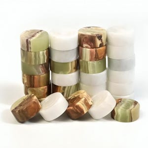 May include: Stacks of polished stone cylinders in shades of white, green, and brown. The cylinders are arranged in neat columns, with some lying on their sides. The stone has a marbled appearance.