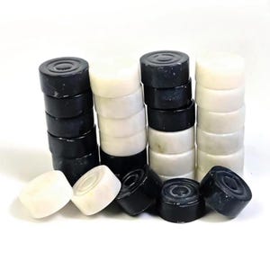 May include: Stacks of black and white game pieces, likely for a board game like checkers or backgammon. The pieces are cylindrical with a slightly concave top, and are arranged in neat columns and scattered around.