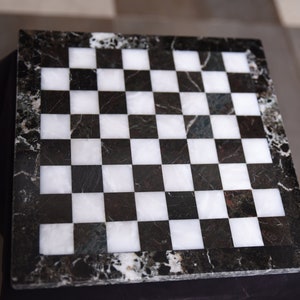 May include: A black and white marble chessboard with a black border. The board is made of polished stone and has a classic checkerboard pattern.