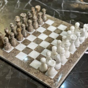 May include: A marble chess set with white and brown pieces on a brown and white marble chessboard.