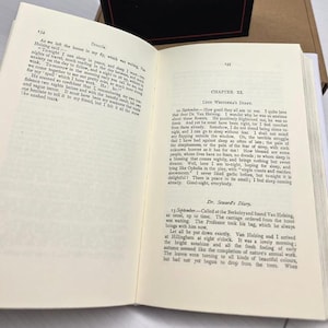 Puede incluir: Un libro de tapa dura abierto que muestra las p&aacute;ginas 134 y 135 de la novela Dr&aacute;cula. El texto incluye el cap&iacute;tulo XI, el diario de Lucy Westenra y el diario del Dr. Seward, impresos en tinta negra sobre papel blanco con tipograf&iacute;a serif.
