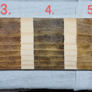 May include: Seven wood samples stained with different shades of brown, labelled 1 through 7. The samples are arranged horizontally on a white surface.