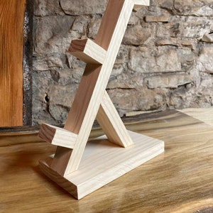 May include: A wooden stand with a unique geometric design, ideal for displaying small items such as jewellery or figurines. The stand is made from natural wood and has a light brown colour.