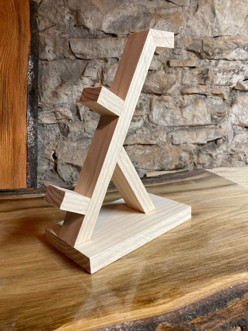 May include: A wooden stand with a unique geometric design, ideal for displaying small items such as jewellery or figurines. The stand is made from natural wood and has a light brown colour.