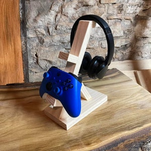 May include: A wooden stand with a blue video game controller and black headphones. The stand is made of natural wood and has a simple design.