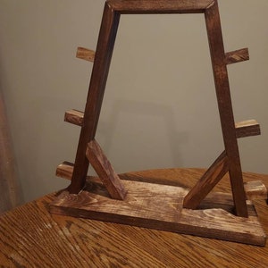 May include: A wooden stand with a triangular frame and multiple shelves. The stand is stained a dark brown colour.