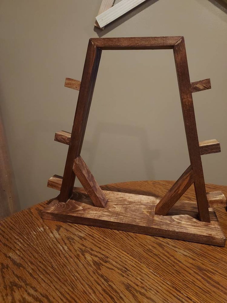May include: A wooden stand with a triangular frame and multiple shelves. The stand is stained a dark brown colour.