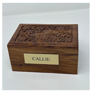 Puede incluir: Una caja de madera con una talla floral en la parte superior. La caja tiene una placa de nombre de latón que dice "CALLIE".
