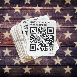 May include: A stack of white paper cards with a QR code and the text "register or check your voter registration: vote.gov". The cards are on a background of a faded American flag.