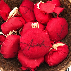 Puede incluir: Una cesta de mimbre llena de bolsitas de tela roja, cada una con la palabra "Aveda" escrita en cursiva negra.