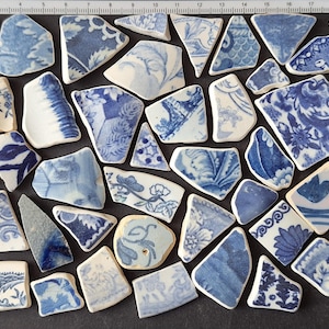 Puede incluir: Una colección de fragmentos de cerámica azules y blancos con varios diseños florales y abstractos. Las piezas varían en tamaño y forma, creando una disposición similar a un mosaico. La paleta de colores es principalmente azul y blanco.