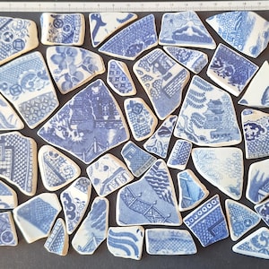 Könnte beinhalten: Eine Ansammlung von blau-weißen Porzellanscherben mit verschiedenen Mustern, darunter Blumen-, geometrische und Landschaftsdesigns. Die Fragmente sind auf einer dunklen Oberfläche angeordnet, die die komplizierten Details des zerbrochenen Geschirrs zeigt.
