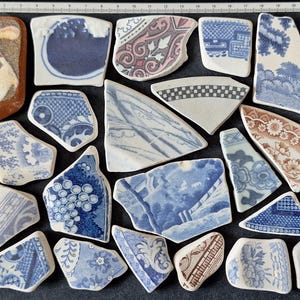 May include: A selection of antique ceramic fragments, showcasing diverse blue and white patterns, such as floral, geometric, and landscape motifs. One shard displays a bird illustration. The pieces vary in shape and size.