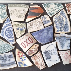 Peut inclure: Une collection d'éclats de céramique anciens, présentant divers motifs et couleurs, dont des motifs floraux et le texte "OXO". Les fragments, dans des tons de bleu, blanc, marron et vert, créent une esthétique vintage.
