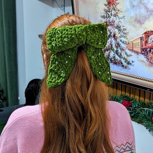 Può includere: Un fiocco di velluto verde con accenti di perle bianche, indossato nei capelli di una donna.