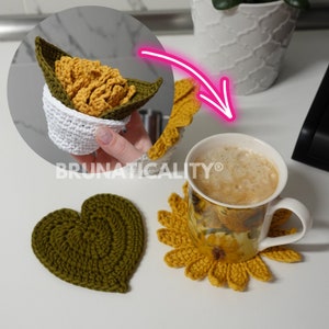 Puede incluir: Artículos de ganchillo que incluyen un cuenco blanco con un soporte en forma de hoja verde, un posavasos de girasol amarillo y un posavasos en forma de corazón verde. Una taza con un diseño floral descansa sobre el posavasos de girasol. El texto "BRUNATICALITY" es visible.