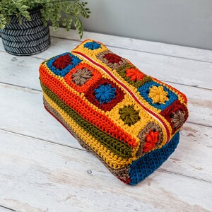 Puede incluir: Una bolsa de cremallera de ganchillo colorida con un patr&oacute;n geom&eacute;trico en tonos de rojo, naranja, amarillo, verde, azul y marr&oacute;n.