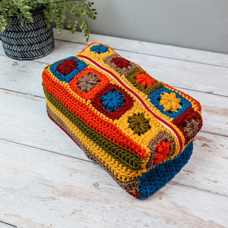 Puede incluir: Una bolsa de cremallera de ganchillo colorida con un patr&oacute;n geom&eacute;trico en tonos de rojo, naranja, amarillo, verde, azul y marr&oacute;n.