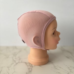 Può includere: Un berretto da notte in rete rosa, realizzato in tessuto morbido ed elastico. Il berretto ha una lunga patta che copre le orecchie e il collo.