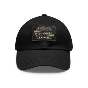 May include: Black baseball cap with a curved brim. The cap features a rectangular patch with the words "American Legendary Corvette 1966 Made in USA" in a gold and white design.