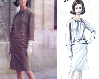 May include: A vintage Vogue Paris Original sewing pattern, number 1445, by Balmain. The pattern features a two-piece outfit with a skirt and a top. The model is wearing a white version of the outfit on the right side of the image, and a brown version on the left side.