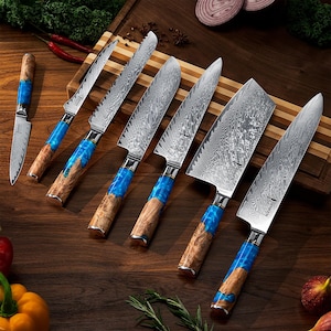 Può includere: Un set di otto coltelli da cucina con manici blu e marroni. I coltelli hanno una lama in acciaio damascato con finitura martellata. I coltelli sono disposti su un tagliere di legno.
