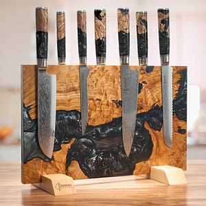 May include: A set of eight black and silver kitchen knives with wooden handles are displayed on a wooden and black resin magnetic knife holder. The holder has the text "Benken Knives" on the bottom.