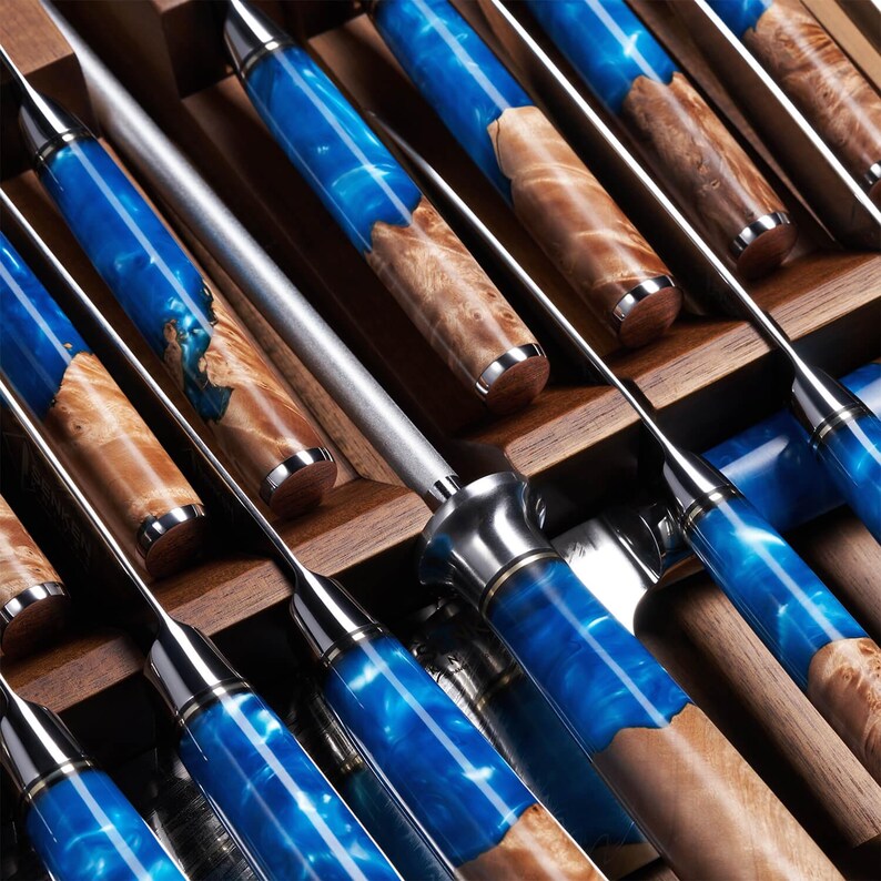 May include: A collection of kitchen knives with stainless steel blades and handles. The handles are a mix of blue resin and wood grain. The knives are displayed in a wooden box, highlighting their distinctive design and craftsmanship.