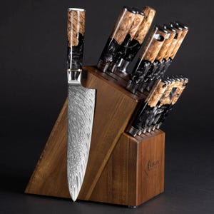 May include: A set of kitchen knives in a wooden block. The knives have patterned steel blades and handles with a mix of black and light brown wood grain. The wooden block is a warm brown color.