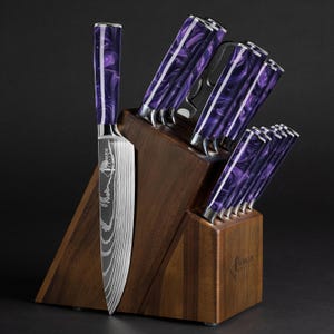 May include: A set of kitchen knives with purple and white marbled handles, displayed in a wooden block. The knives have silver blades and are arranged in a dark setting. The brand name "NUMKEN" is visible on the knife and the block.