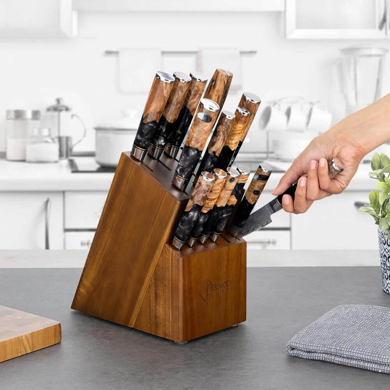 May include: A wooden knife block with a set of knives. The knives have brown and black handles and silver blades. The block is made of wood and has a slanted design. A hand is removing a knife from the block.