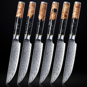 Peut inclure: Ensemble de six couteaux à steak. Les lames présentent un motif détaillé. Les manches combinent du bois brun clair et de la résine noire. Chaque couteau a une mitre argentée et un accent doré. Disposition en ligne.