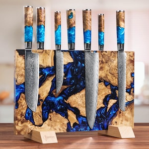 Könnte beinhalten: Ein Set aus sechs Küchenmessern mit gemusterten Klingen und Griffen. Die Griffe sind eine Kombination aus Holz und blauem Harz. Die Messer werden in einem Holzblock mit blauem Harzdesign präsentiert. Der Holzblock hat einen Holzsockel.