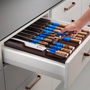 Op de afbeelding: Een set keukenmessen met houten en blauwe hars handvatten, opgeborgen in een houten lade-organizer. De messen hebben zilveren bladen en zijn netjes gerangschikt. De merknaam "SENKEN" is zichtbaar.