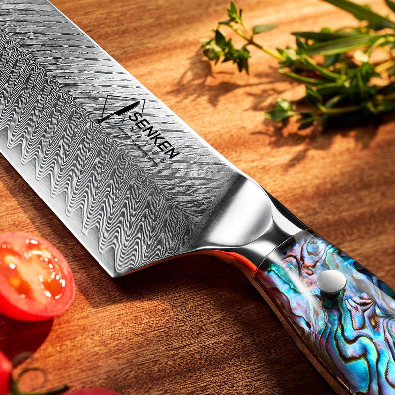 May include: A silver chef's knife with a black and blue patterned handle. The blade has a wavy pattern and the text "SENKEN" is printed on the blade.