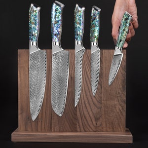 May include: A set of six kitchen knives with mother-of-pearl handles are displayed in a wooden magnetic knife holder. The knives have a silver blade with a textured pattern.