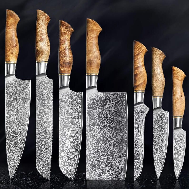 A set of seven kitchen knives with patterned Damascus steel blades and light brown burl wood handles. The collection includes various blade shapes, such as a cleaver, chef's knives, and paring knives, all featuring silver bolsters.