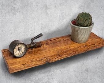 Puede incluir: Una estantería rústica de madera con un manómetro vintage y un pequeño cactus en maceta. La estantería es de madera envejecida con vetas y nudos visibles. El manómetro tiene un mango negro y una esfera blanca. El cactus es verde y espinoso.