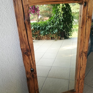 Puede incluir: Un espejo de madera r&uacute;stico con un marco rectangular. El marco est&aacute; hecho de madera recuperada con un acabado marr&oacute;n natural. El espejo refleja una vista de un patio con plantas verdes y un suelo de piedra.