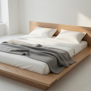 Puede incluir: Una cama moderna con plataforma y marco de madera clara. La cama est&aacute; hecha con s&aacute;banas blancas, dos almohadas blancas y una manta gris. La habitaci&oacute;n es luminosa y minimalista.