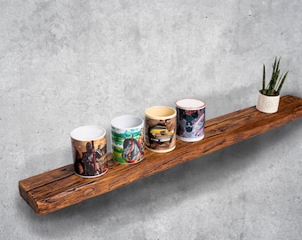 Puede incluir: Cinco tazas de cerámica con diferentes diseños se colocan en un estante de madera rústico. El estante está montado en una pared de concreto gris. Una pequeña planta en maceta se encuentra en el estante a la derecha de las tazas.