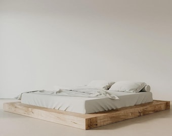 May include: A minimalist bed frame with a light-colored mattress and pillows. The bed sits on a natural wood platform. The bedding is a light gray color, creating a serene and modern aesthetic.