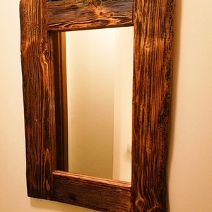 Puede incluir: Un espejo de madera r&uacute;stico con un acabado marr&oacute;n oscuro. El marco est&aacute; hecho de madera recuperada con un patr&oacute;n de veta de madera natural. El espejo es rectangular y tiene un dise&ntilde;o simple.