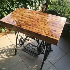 Peut inclure: Un plateau de table en bois avec une finition époxy transparente, posé sur un piétement de machine à coudre Singer en métal noir.
